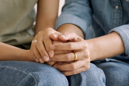 Two sets of hands are clasped together in one person's lap.