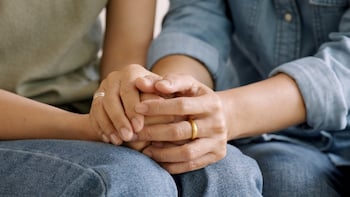 An image of two sets of hands clasped together in a person's lap.