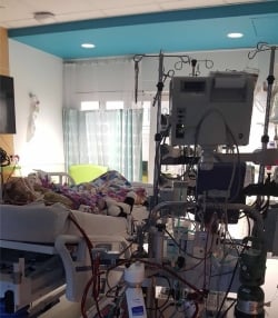 A patient in a hospital bed with many machines and a colorful blanket.