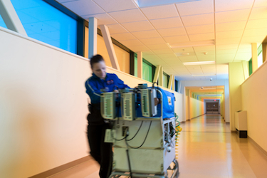 A bridge connects University Health Truman Medical Center to Children's Mercy for patients who need care in our NICU or Fetal Health Center. The bridge features colorful glass panels. A CMKC Transport Team member moves quickly to bring a baby in an isolette from UHTMC to CMKC.