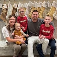 Ashlyn Johnson in white shirt with her three children wearing red shirts and her husband in grey shirt sitting on a couched bench