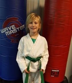 A young girl with blond hair in a karate uniform with a green belt.