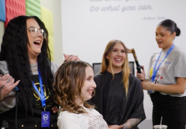 Two hairstylists style the hair of two teenage girls.