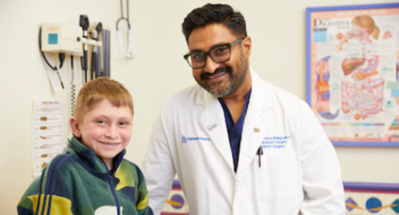 A redheaded boy sits on an exam table next to a physician wearing a white coat.