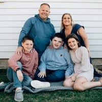 Rob and Heidi Burns in blue posing with their three children outside 