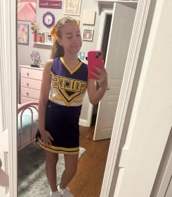 A preteen girl takes a selfie in a blue and yellow cheerleading uniform.