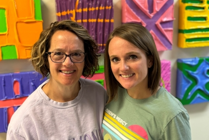 Two women pose together in front of colorful artwork