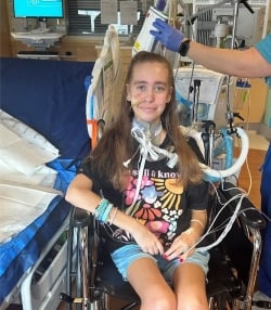 A preteen girl sits in a wheelchair while connected to an ECMO device.