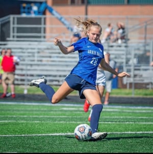 A teenage girl with a blond ponytail kicks a soccer ball