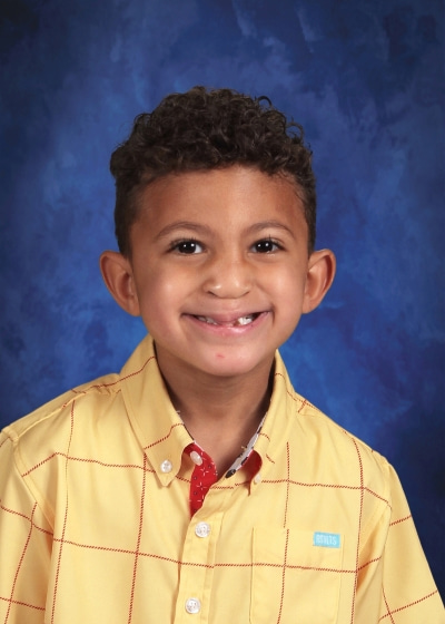 An 8-year-old boy with curly brown hair poses for a school photo.