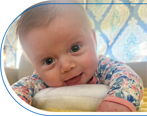 Baby Brexley laying on her stomach and smilng while looking into the camera.