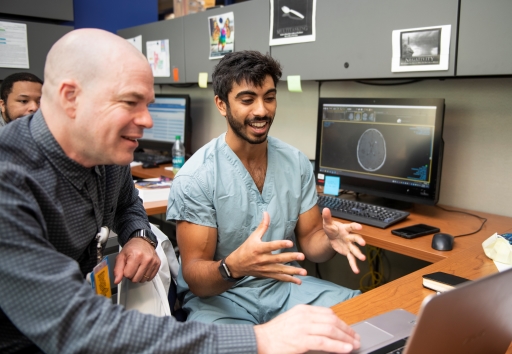 Two men look at a computer screen together. One is white with no hair, and one has brown skin with dark hair and a beard.