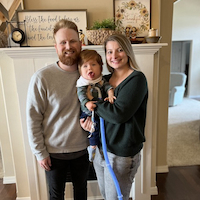 Lauren Ward, standing with child and husband in home. 