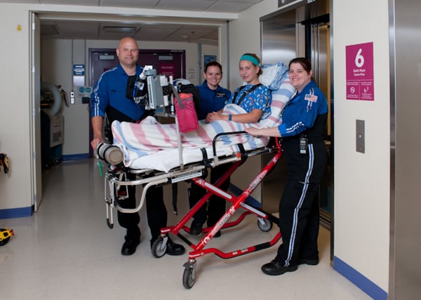 Three members of transport team in blue and black uniforms arriving with patient in EMT gurney