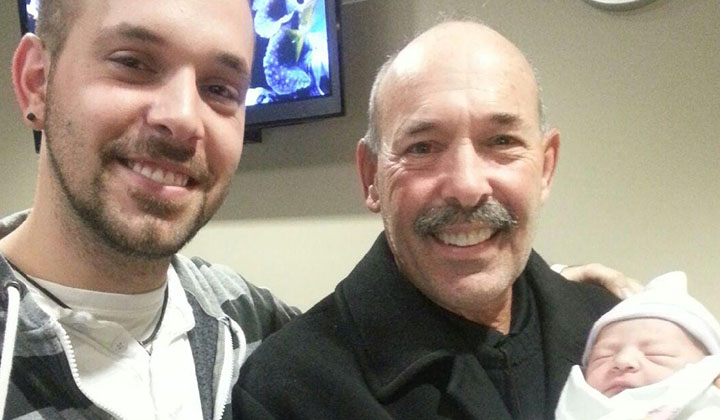 Dad and grandpa smiling while holding newborn