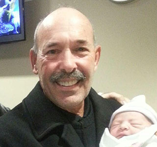 Dad and grandpa smiling while holding newborn