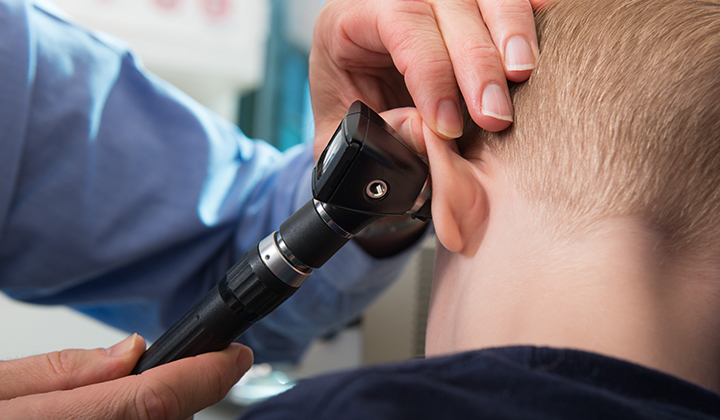 Close up of a child's back of the head while a doctor uses an otoscope to look in his ear.