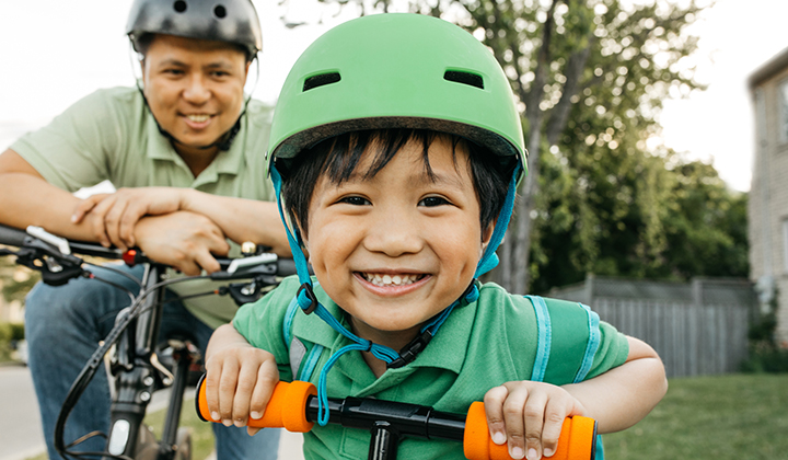 Child on bike smiling with Dad following behind