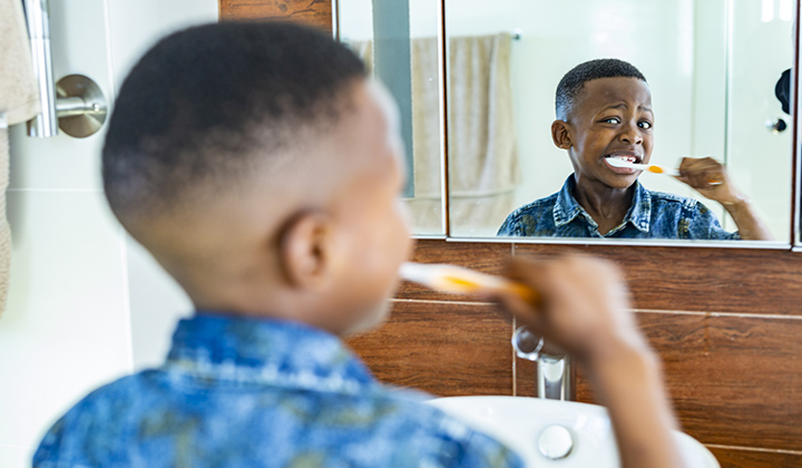 Young child looking in a mirror while brushing his teeth.