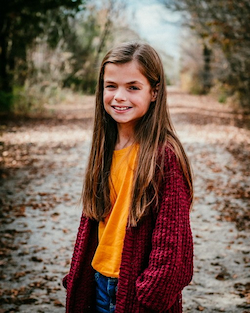 Young girl Kaydee stands wearing a red cardigan