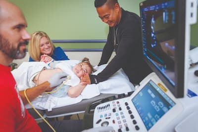 Mayia’s parents, Misti and Roy, hold her hand while Tyler Johnson conducts a procedure during her quarterly heart check at Children’s Mercy.